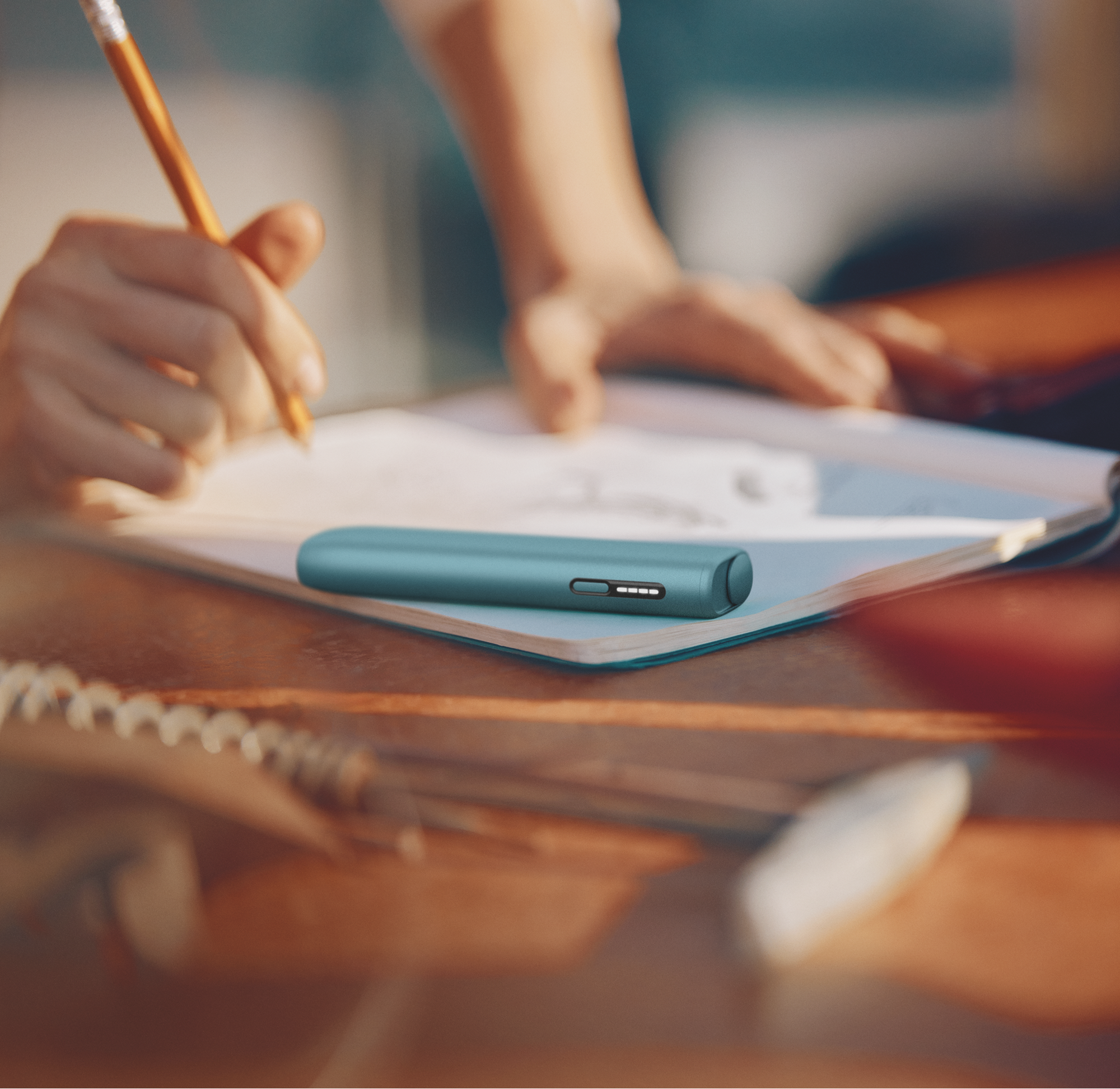 IQOS ILUMA i ONE color breeze blue sobre una cuaderno